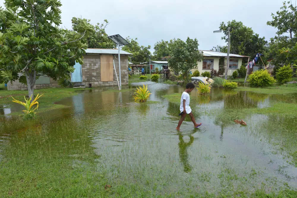 Uma menina indígena fijiana caminha em terreno alagado em Fiji. A ilha foi duramente castigada por inundações causadas por um ciclone tropical, um dos impactos do aquecimento dos oceanos.