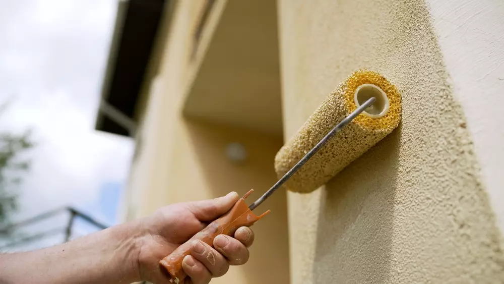 Pessoa pintando a parede de uma residência com um rolo de pintura, demonstrando o impacto do Programa Reforma Casa Brasil na transformação social por meio da habitação.