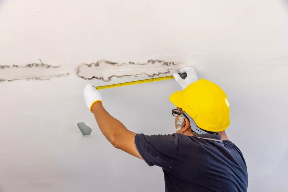 Profissional analisando infiltração e problemas na estrutura do teto que podem contribuir para a Síndrome do Edifício Doente, destacando fatores de saúde e segurança.