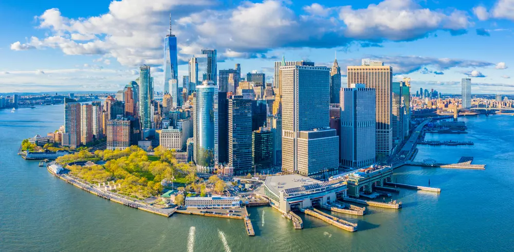 Vista aérea do centro de Manhattan com foco no conceito 'The Big U' entre proteção e acolhimento, destacando arranha-céus, o rio Hudson e o parque ao redor.