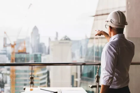 Profissional de construção civil analisando projeto de Lean Construction em um ambiente moderno de escritórios com vista para a cidade