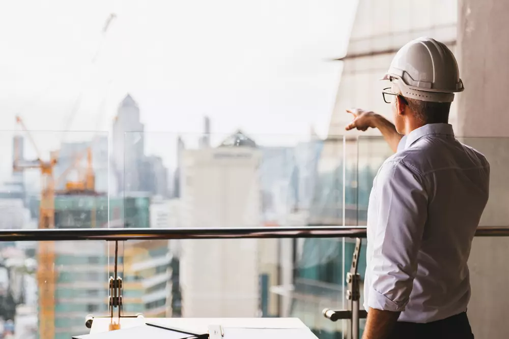 Profissional de construção civil analisando projeto de Lean Construction em um ambiente moderno de escritórios com vista para a cidade