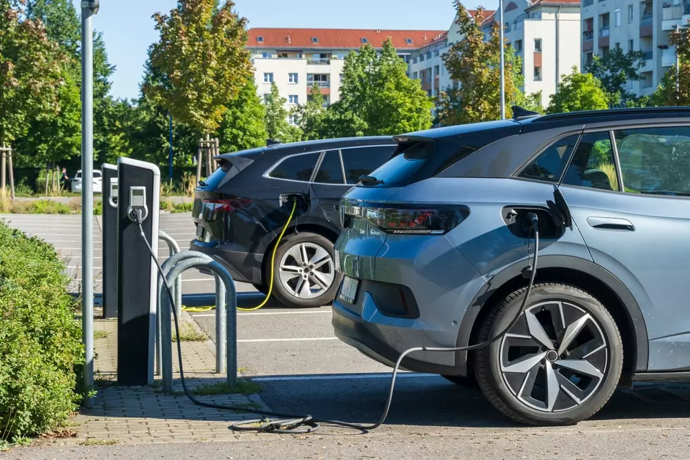 Carros elétricos carregando em um bairro sustentável, rodeados por áreas verdes e árvores, promovendo uma redução de emissões de carbono.