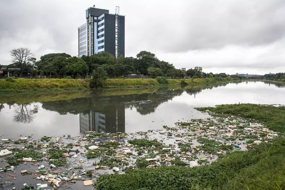 Um rio poluído com lixo flutuante, destacando a necessidade urgente de reduzir a poluição dos rios.