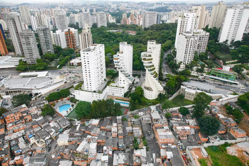 Vista aérea de condomínios altos e área residencial de baixa demanda em uma cidade brasileira, com muitas áreas verdes ao fundo.