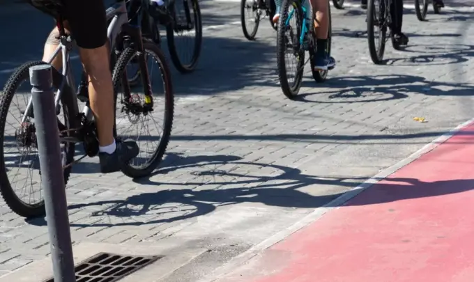 Grupo de ciclistas pedalando em ciclovia pavimentada, promovendo transporte sustentável e saúde em área urbana com sombra.