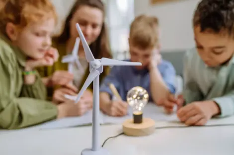 Crianças participando de uma atividade educativa sobre energias renováveis em sala de aula, com foco na adaptação climática das cidades usando fontes sustentáveis.