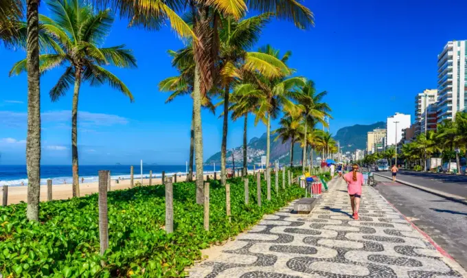 Dia ensolarado na orla da praia de Ipanema, com uma pedestre passando. A foto ilustra a matéria sobre a restauração da restinga em Ipanema.